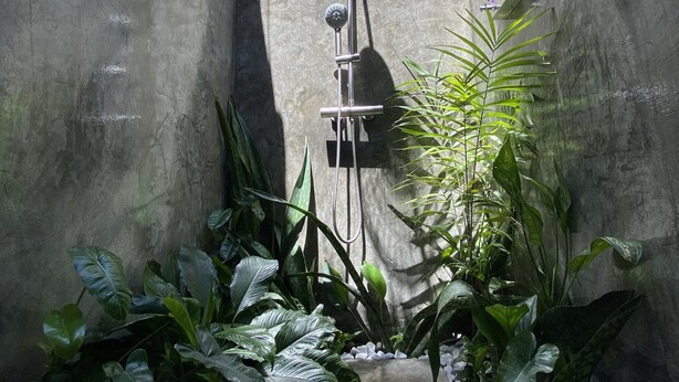 A concrete shower enclosure with a rain showerhead, surrounded by tropical plants and white pebbles. - Wild Monkeys Hostel (Moalboal)