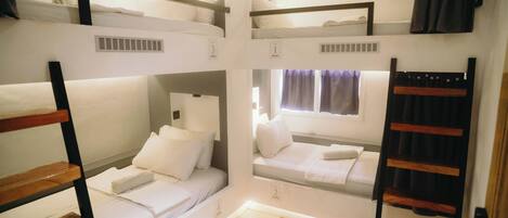 Habitación tipo dormitorio con literas, una ventana con cortinas y un respiradero visible.