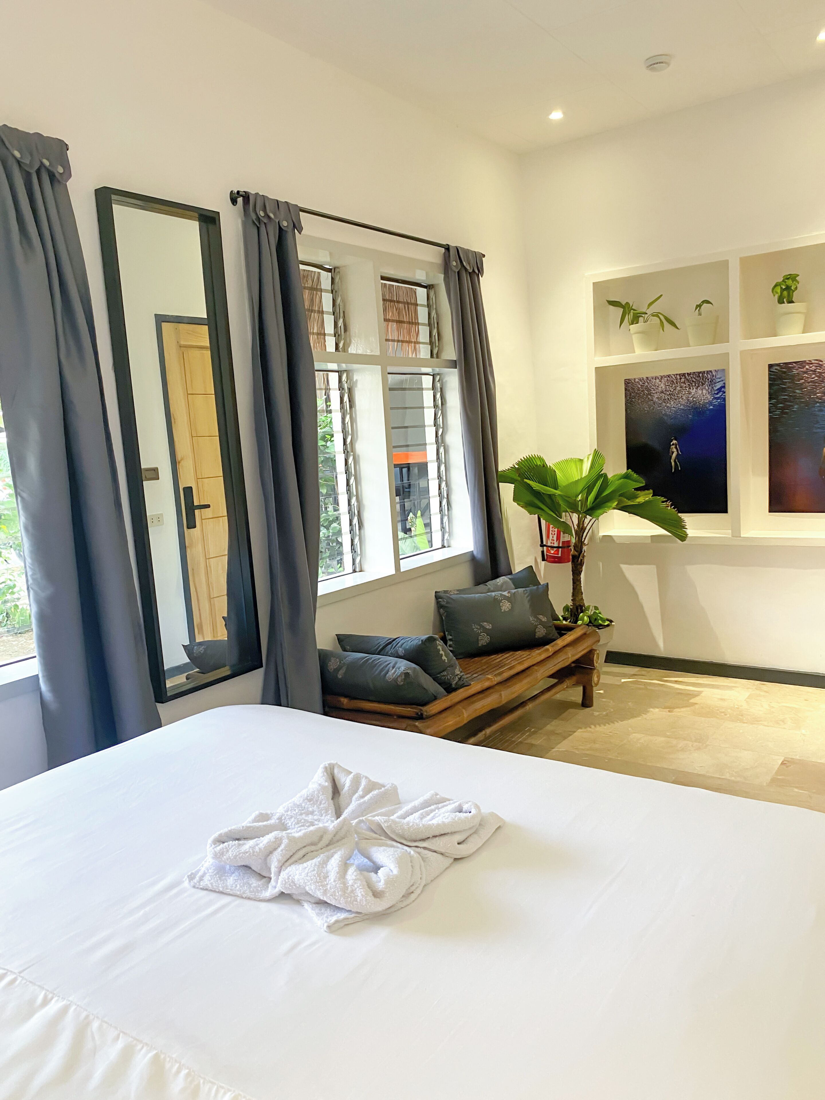 A hotel room with a large bed, a bench with cushions, a potted plant, and artwork on the wall.