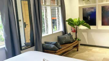 Ein Hotelzimmer mit einem großen Bett, einer Sitzbank mit Kissen, einer Topfpflanze und Kunstwerken an der Wand.