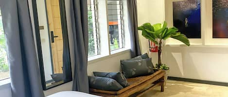 A hotel room with a large bed, a bench with cushions, a potted plant, and artwork on the wall.