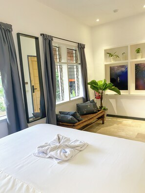 A hotel room with a large bed, a bench with cushions, a potted plant, and artwork on the wall. - Wild Monkeys Hostel (Moalboal)
