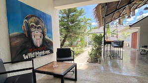 A spacious outdoor area with a concrete floor, a wooden table, and black chairs. There is a large painting of a gorilla on the wall, and a view of a garden with trees and plants. - Wild Monkeys Hostel (Moalboal)