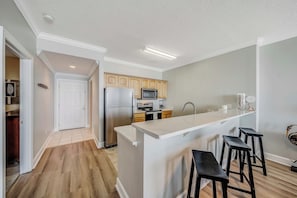 A modern kitchen with a central island, wooden cabinets, a stainless steel refrigerator, and a microwave.