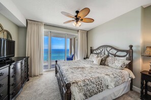 A bedroom with a bed, a television, a ceiling fan, and a view of the ocean through a sliding door. - Ocean Reef 1108 Beachfront, Heated Indoor & Outdoor Pools, Hot Tub, FREE Golf (Panama City Beach)