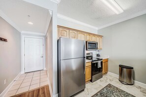 A modern kitchen with stainless steel appliances, wooden cabinets, and a tiled floor. - Ocean Reef 1108 Beachfront, Heated Indoor & Outdoor Pools, Hot Tub, FREE Golf (Panama City Beach)