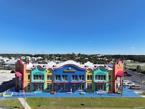 A colorful building with multiple storefronts, a parking lot, and a clear view of the surrounding neighborhood.