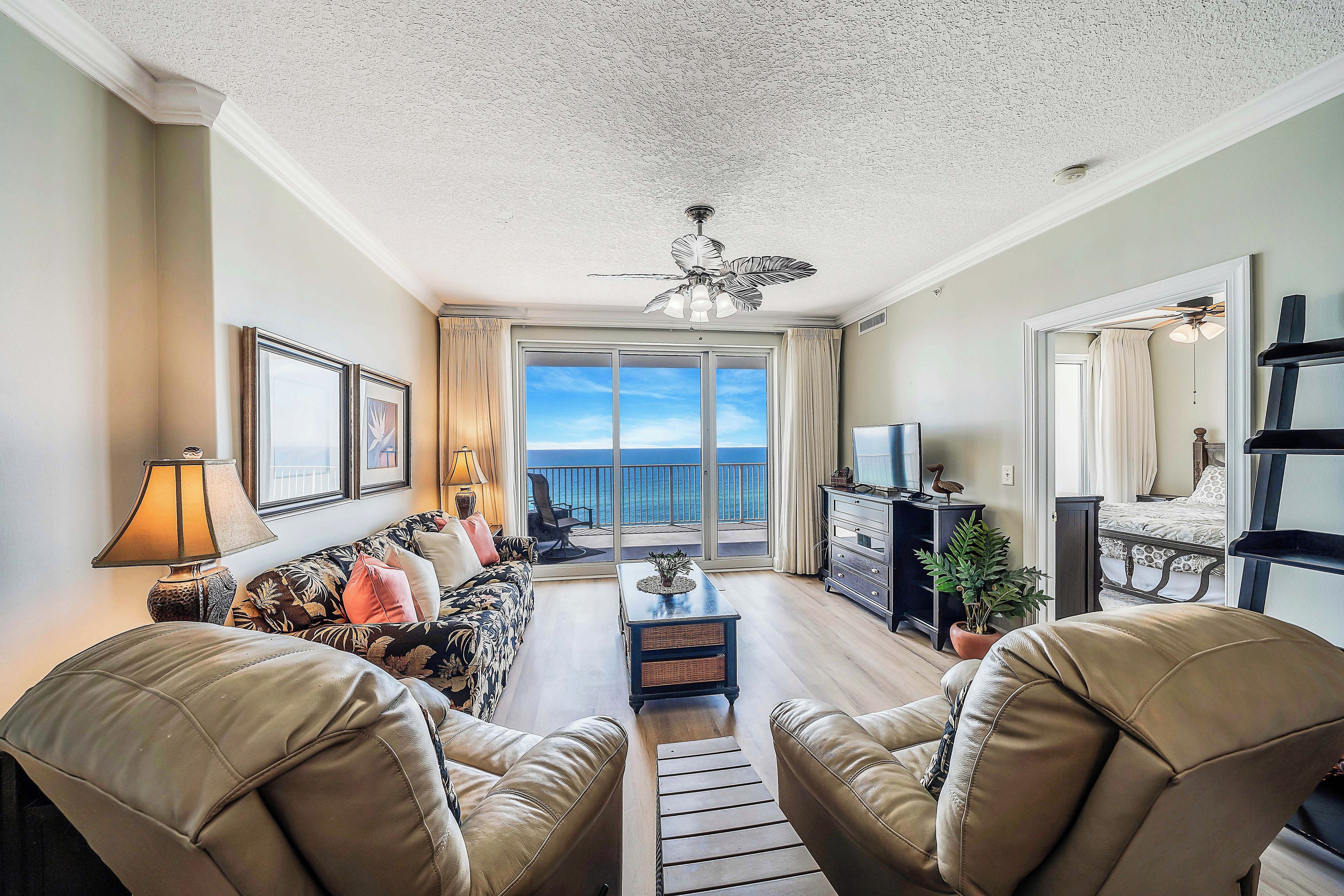 A living room with a sofa, chairs, a TV, a ceiling fan, and a view to the outside.