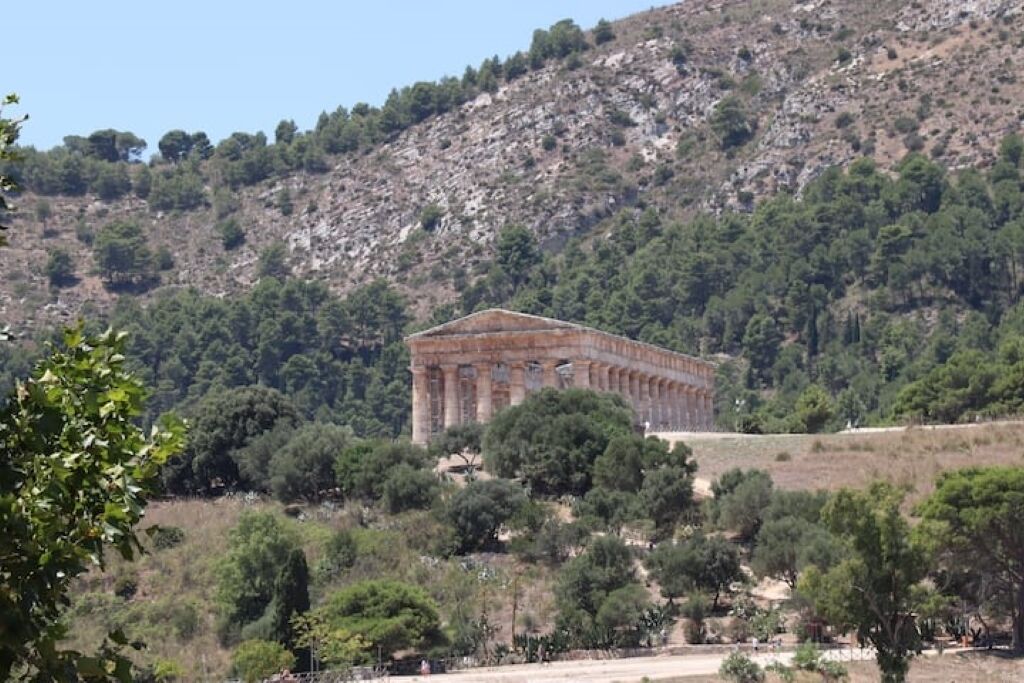 A historical building with columns, surrounded by trees and hills.