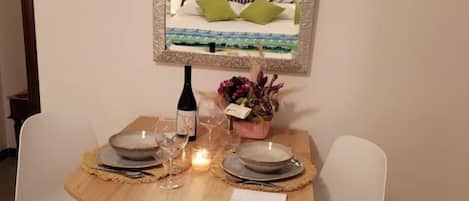 A dining table set with plates, glasses, and a candle, surrounded by white chairs.