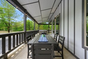An outdoor patio with a table and chairs, a covered area, and a view of trees.