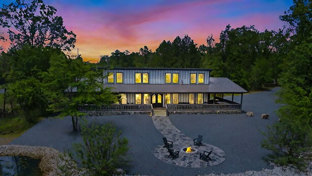 A modern house with a stone patio, a fire pit, and a view of a lake.