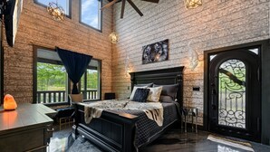 A bedroom with a large bed, a wooden wall, a window, and a door with a decorative glass panel.