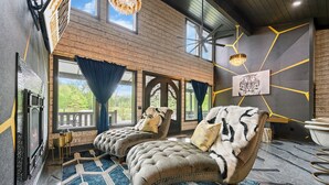 A room with a fireplace, two plush armchairs, a large window with curtains, and a tiger painting on the wall.