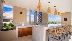 Una cocina moderna con encimera de mármol, armarios de madera y una zona de bar con sillas de mimbre.