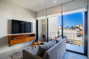Una sala de estar moderna con un televisor de pantalla plana, mueble de entretenimiento de madera, sofá gris y una pequeña mesa redonda.
