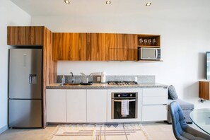 Et moderne køkken med træskabe, et stålkøleskab, en mikrobølgeovn, en gasblus og et glasbord til spisning.