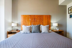 A hotel room with a large bed, a wooden headboard with carvings, two bedside tables with lamps, and a nightstand with a clock.