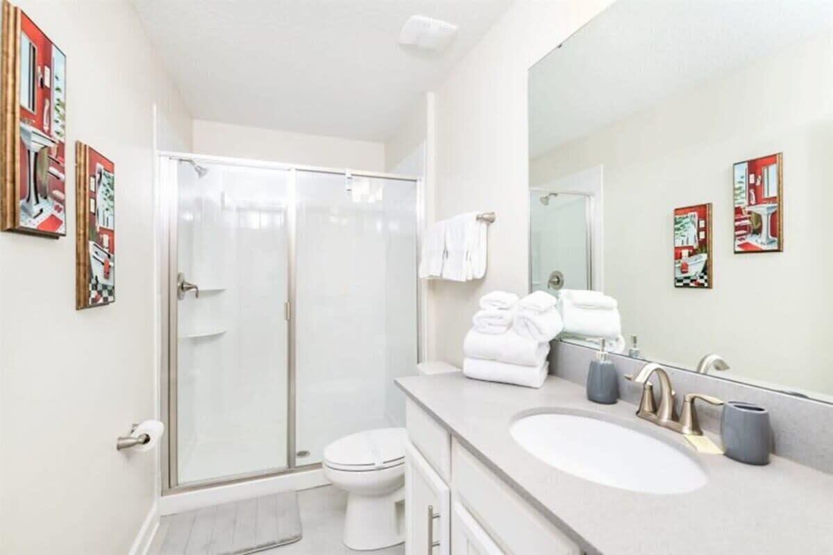 A modern bathroom with a glass shower enclosure, a white toilet, a sink with a vanity, and a large mirror.