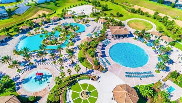 An aerial view of a resort with multiple swimming pools, sun loungers, and palm trees. - ChampionsGate Home · Pool & Game Room Near Disney (Davenport)