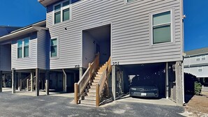 A two-story residential building with a covered parking area and a staircase leading to the entrance. - Dove's Landing | Serene Coastal Retreat + Access to Pool & More! (Surf City)