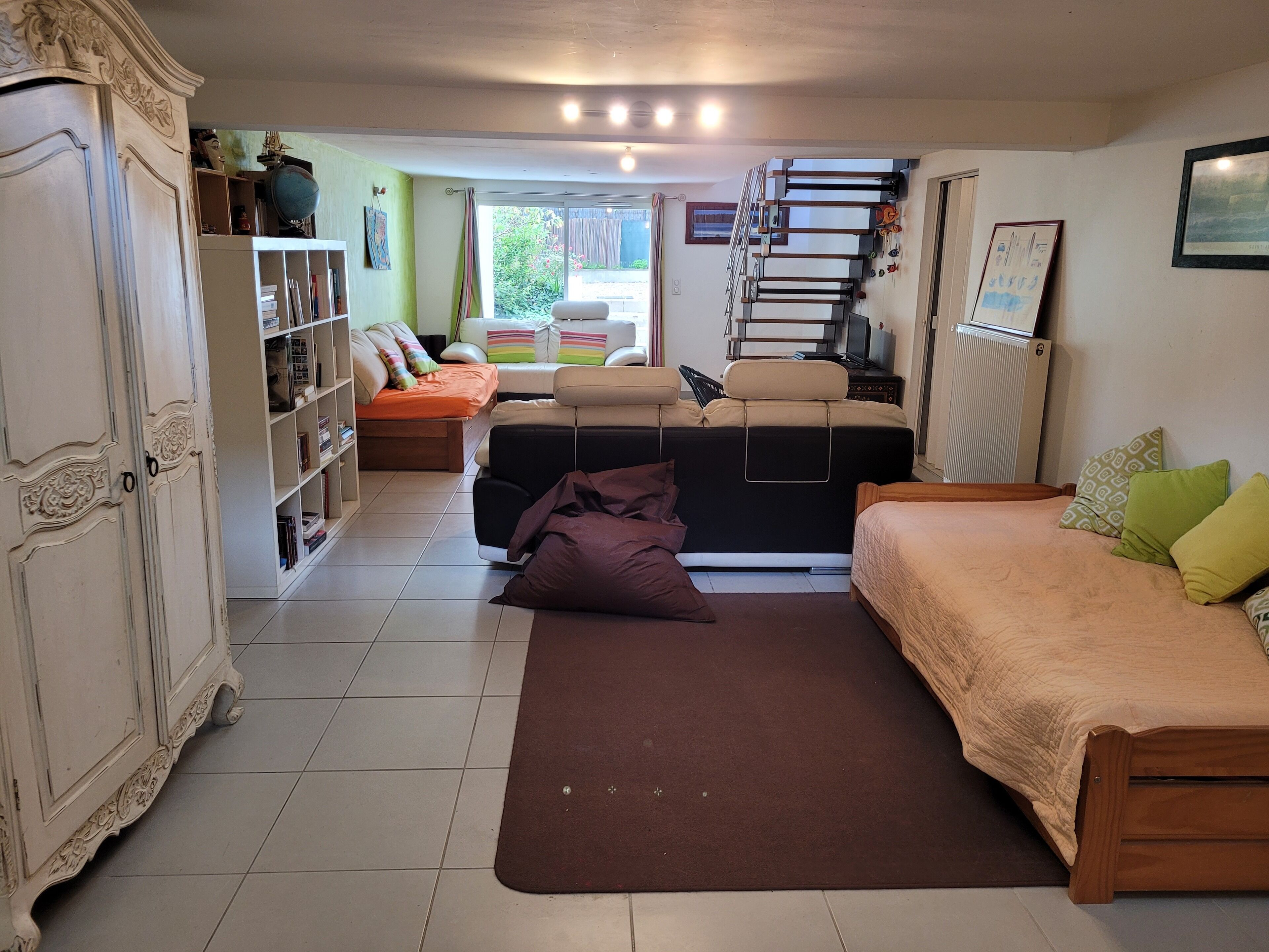 A room with a bed, a sofa, a bookshelf, and a staircase.