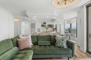 A modern living room with a green sofa, a dining area, and a view of the sea. - Sunset Luxe, 1606 Brighton - full access to amenities! (Myrtle Beach)