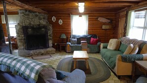 A cozy cabin interior with a stone fireplace, wooden walls, a green sofa, a blue armchair, and a patterned floor.