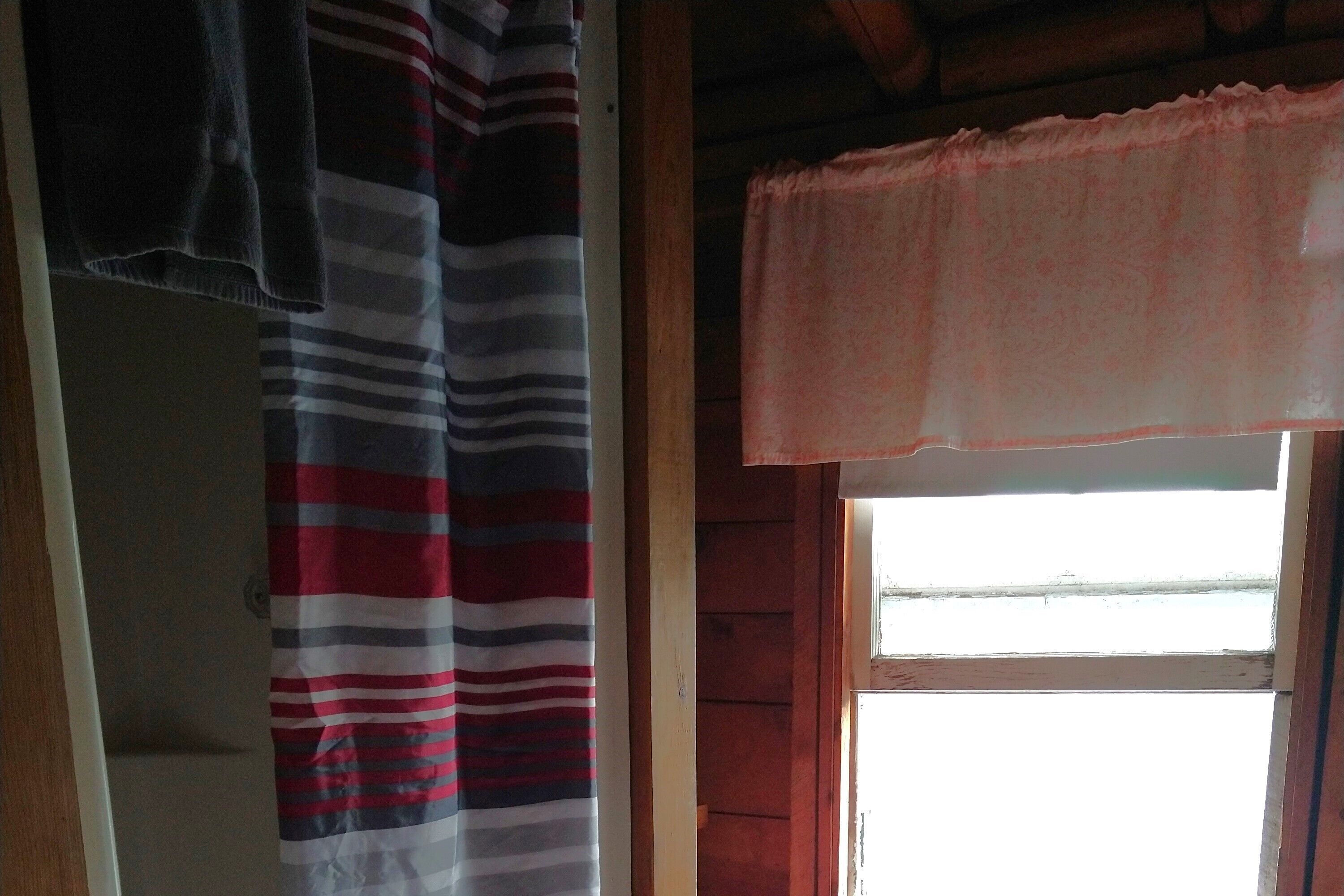 A room with a striped curtain, a window with a pink valance, and wooden walls.