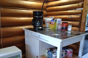 Une petite cuisine équipée d’une machine à café, d’un four à micro-ondes et d’une étagère où sont rangées des tasses.