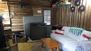 Ein gemütliches Blockhaus mit Holzwand, Kamin, einer Couch mit Kissen, einem Holztisch und einem gemusterten Teppich.