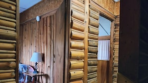 Ein Holzhütten-Interieur mit einer Holzwand, einem Tisch mit Lampe und einem Fenster mit Vorhang.