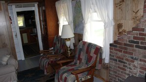A cozy living room with a fireplace, wooden furniture, and a patterned rug. - Rustic, two-story, clapboard cottage, field view, Pet-friendly, Downeast Maine (Edmunds Twp)