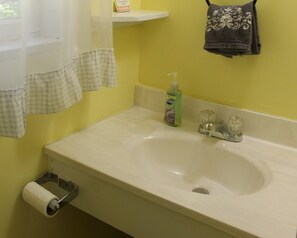 A bathroom with a sink, a toilet paper holder, a soap dispenser, and a towel hanging on the wall.