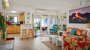 Un grand espace de vie comprenant un canapé, une table basse et une table à manger avec des chaises. Il y a également une cuisine équipée de meubles en bois et d’un réfrigérateur.