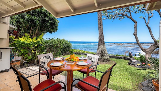 Une terrasse couverte avec une table dressée pour quatre personnes, offrant une vue imprenable sur l’océan.