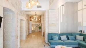 A spacious living area with a teal sofa, stone walls, and a staircase leading to an upper level. - Luxury Apartment (Jerusalem)