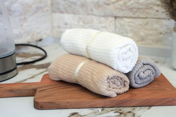 A wooden cutting board with three rolled towels in beige, white, and gray colors. - Luxury Apartment (Jerusalem)