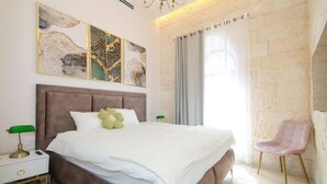A modern bedroom with a large bed, a nightstand, a chair, and abstract wall art. - Luxury Apartment (Jerusalem)