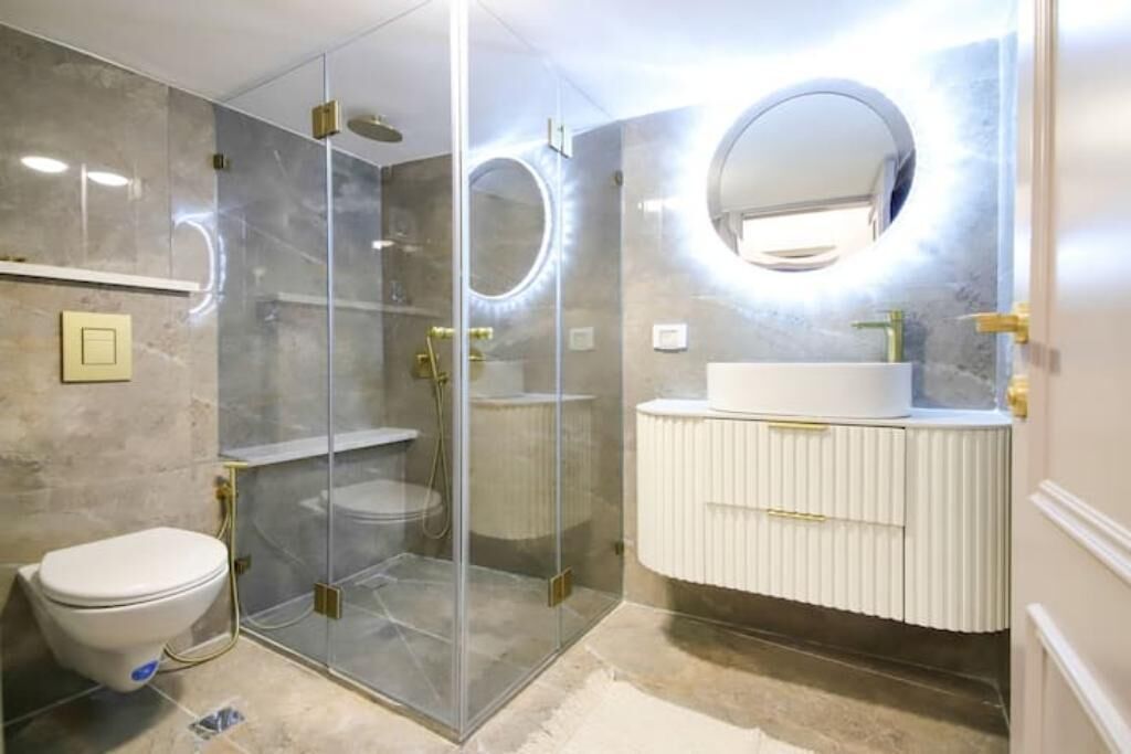 Une salle de bain moderne avec une douche à parois de verre, un lavabo blanc et un miroir rond.