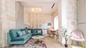 A modern living room with a teal sofa, a round coffee table, and a dining area with a pink chair. - Luxury Apartment (Jerusalem)