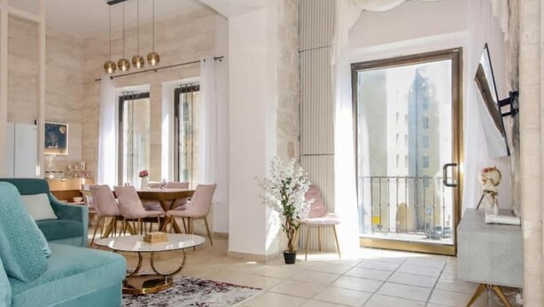 A spacious living room with a teal sofa, a round coffee table, and a dining area with pink chairs. - Luxury Apartment (Jerusalem)