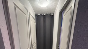 Un couloir étroit avec des portes blanches, un rideau noir et un luminaire au plafond.
