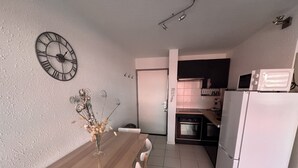 Une cuisine compacte avec un réfrigérateur blanc, un four à micro-ondes et une cuisinière. On y trouve une table à manger avec des chaises et une horloge décorative au mur.