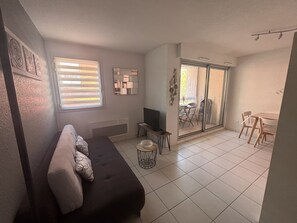 Cozy living space with a sofa, side table, and TV, leading to an outdoor dining area.