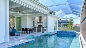 A pool area with a covered patio, seating, and a kitchen area.