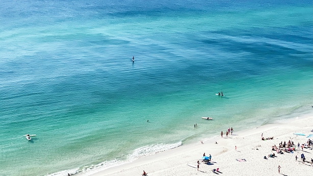 A beach with clear turquoise water, a sandy shore, and people engaging in various activities. - HUGE Corner Unit Free Beach Chairs! Free round of Golf & Activities Daily! (Panama City Beach)