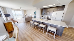 A modern kitchen with a central island, bar stools, and a view to the outside. - HUGE Corner Unit Free Beach Chairs! Free round of Golf & Activities Daily! (Panama City Beach)