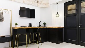 Una cocina moderna con encimera negra, taburetes dorados, un lavamanos negro y un televisor de pantalla plana montado sobre la encimera.