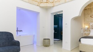 Un dormitorio moderno con un ventanal grande, una bañera, una cama y una pequeña mesa redonda.